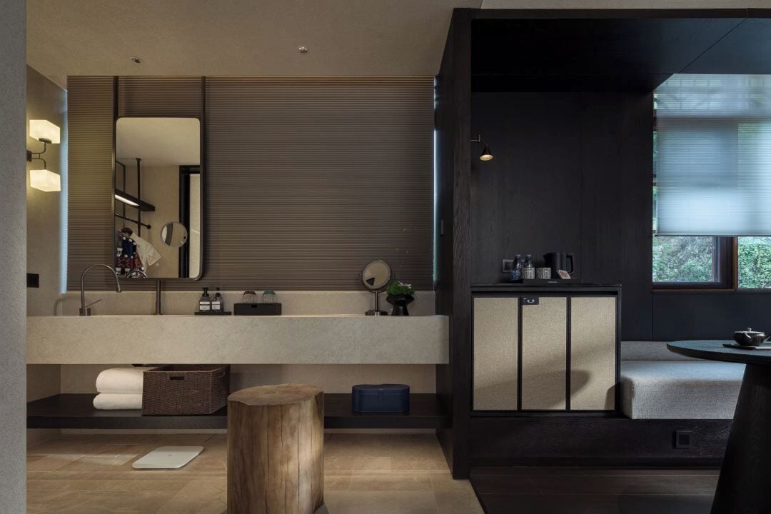A modern bathroom with a large mirror, a sink, and a cabinet. There is a wooden stool and a small table with a cup.