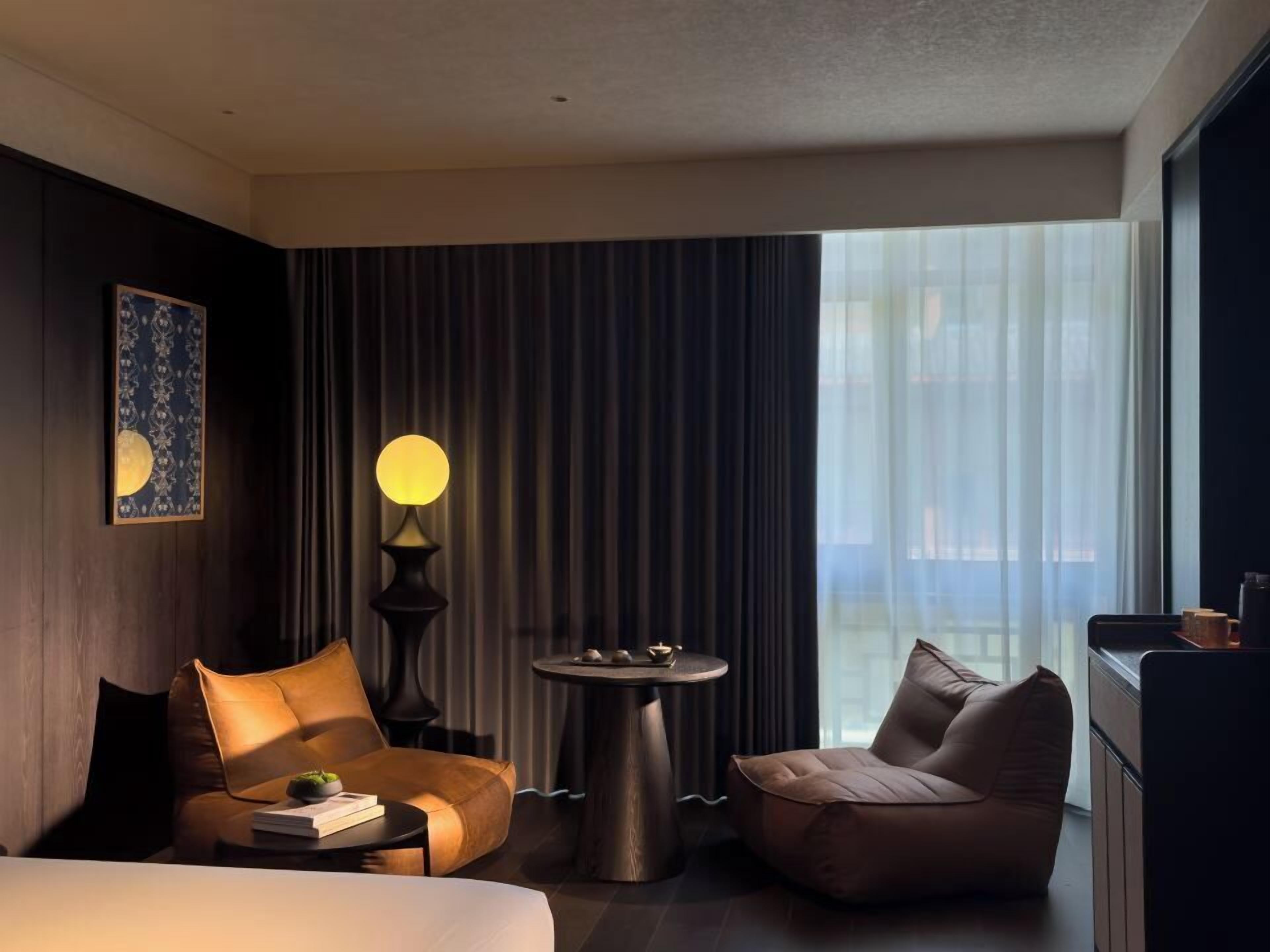 A modern hotel room with a large bed, two sofas, a round table, and a lamp.