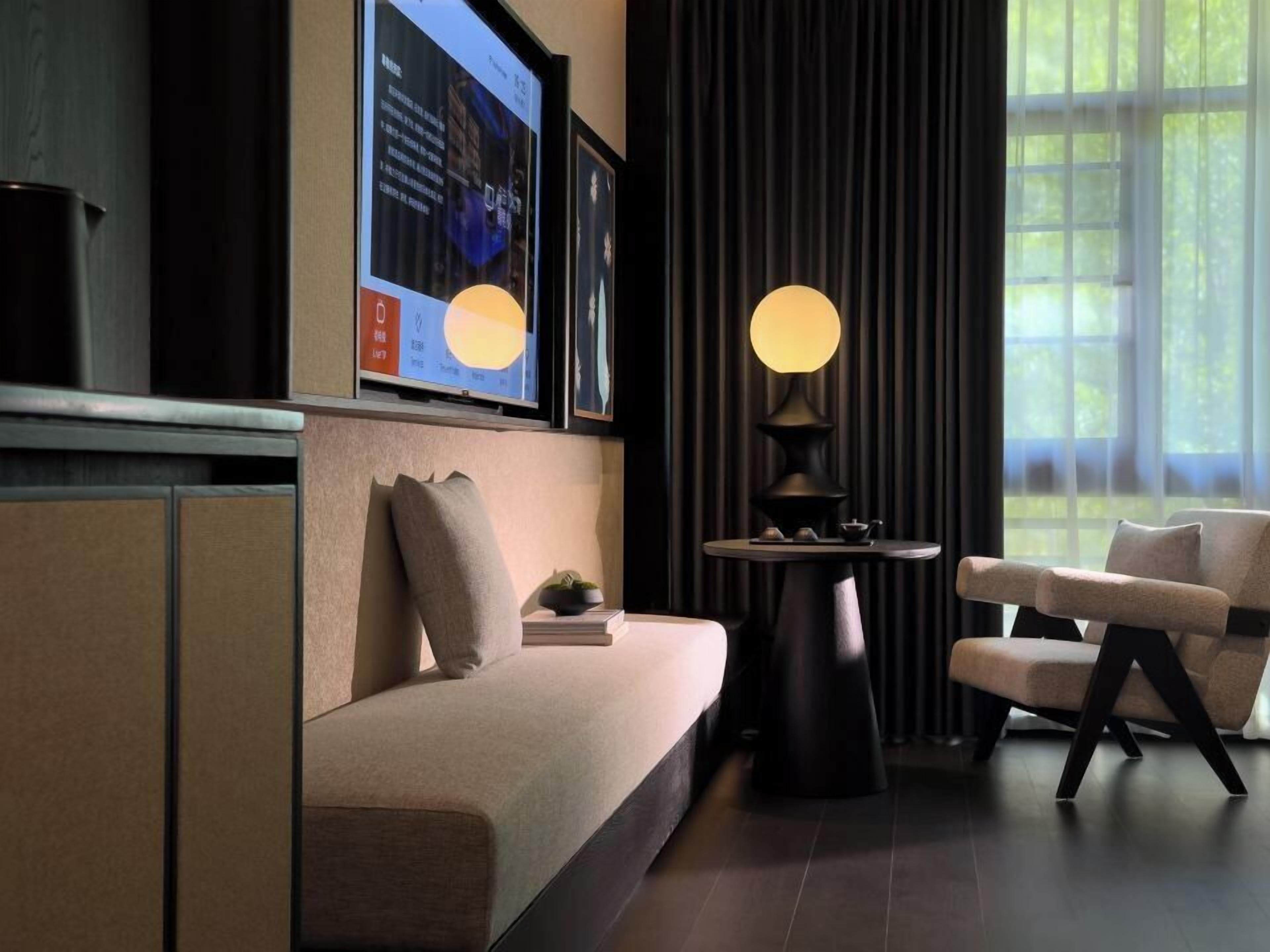 A modern living room with a sofa, a round table with a lamp, and a television mounted on the wall.