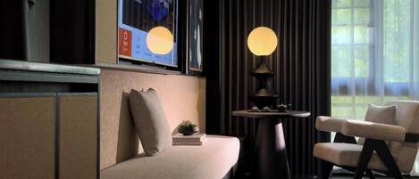 A modern living room with a sofa, a round table with a lamp, and a television mounted on the wall.