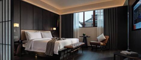 Una habitación de hotel moderna con una cama grande, un escritorio pequeño, una silla y un ventanal con cortinas.