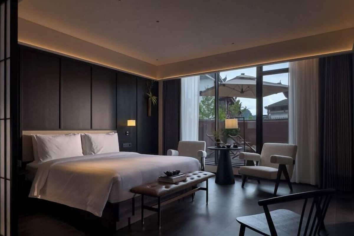 Une chambre d’hôtel moderne, dotée d’un grand lit, d’une petite table avec des chaises et offrant une vue sur l’extérieur.