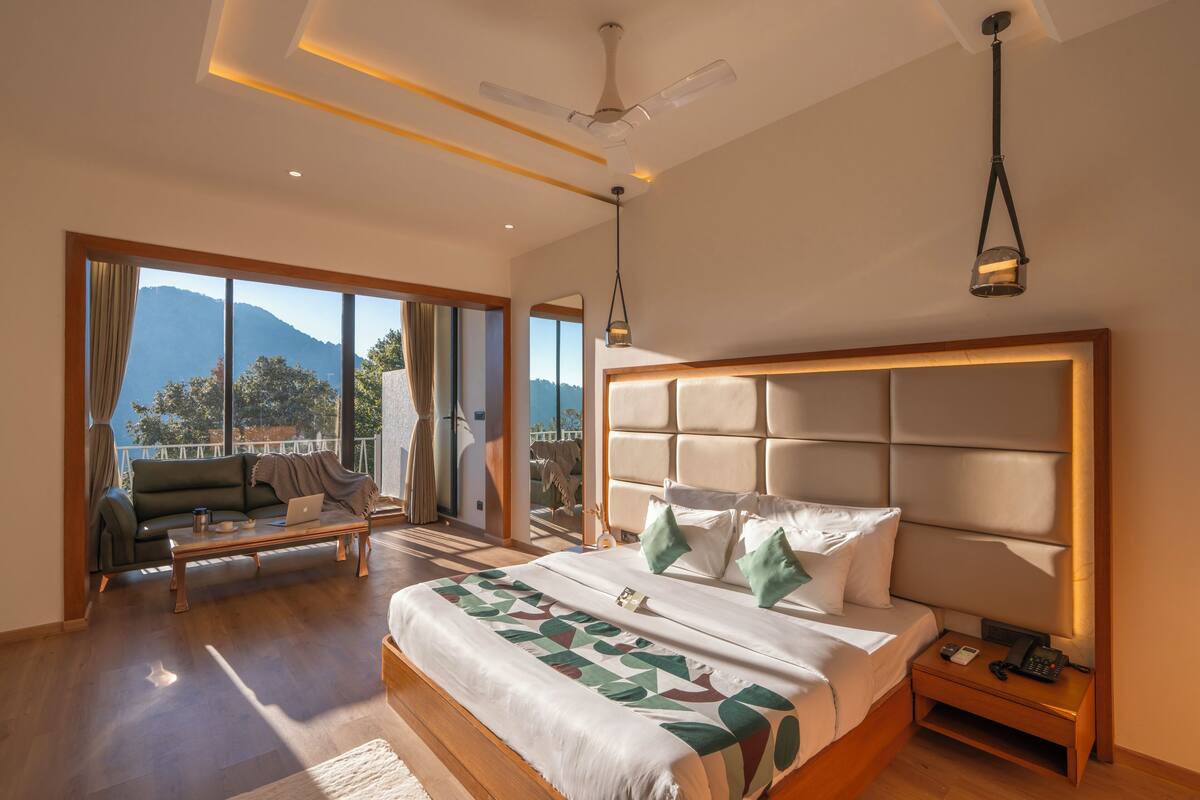 A modern hotel room with a large bed, a sofa, and a balcony with a mountain view.