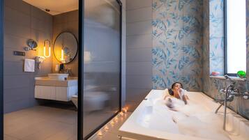 Un baño moderno con una bañera grande, un espejo, un lavabo y un inodoro. Hay velas en el suelo y una ventana con vistas.