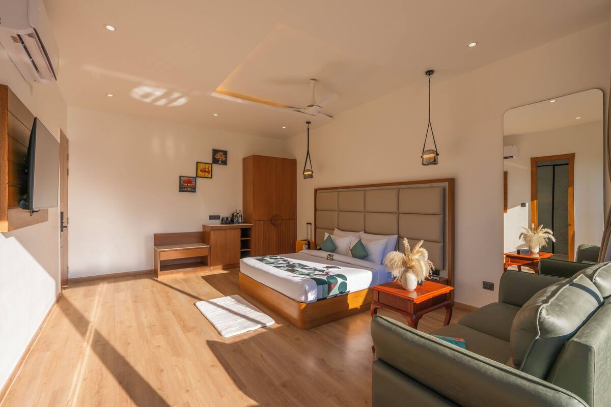 A modern bedroom with a wooden floor, a bed with a headboard, a bedside table, a mirror, and a sofa.