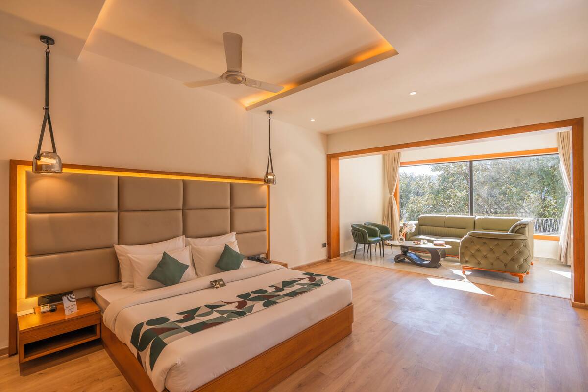 A modern hotel room with a large bed, a ceiling fan, and a balcony with seating.