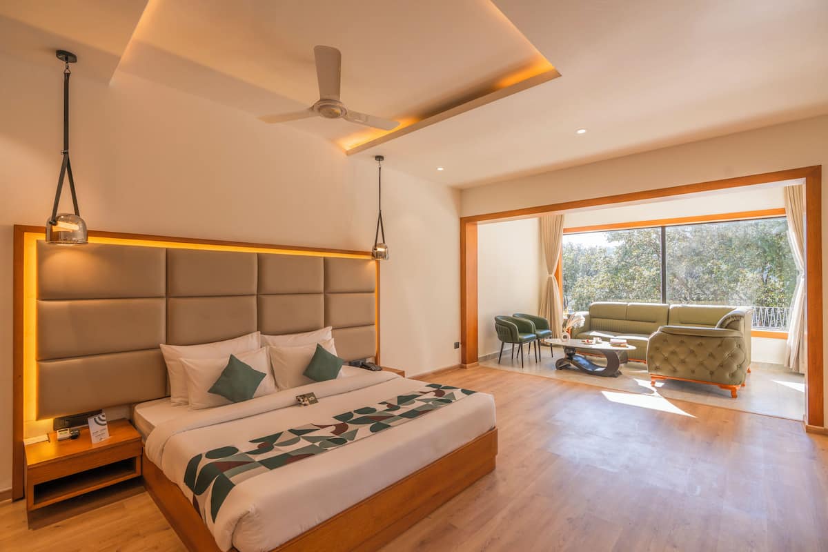 A modern hotel room with a large bed, a ceiling fan, and a balcony with seating.