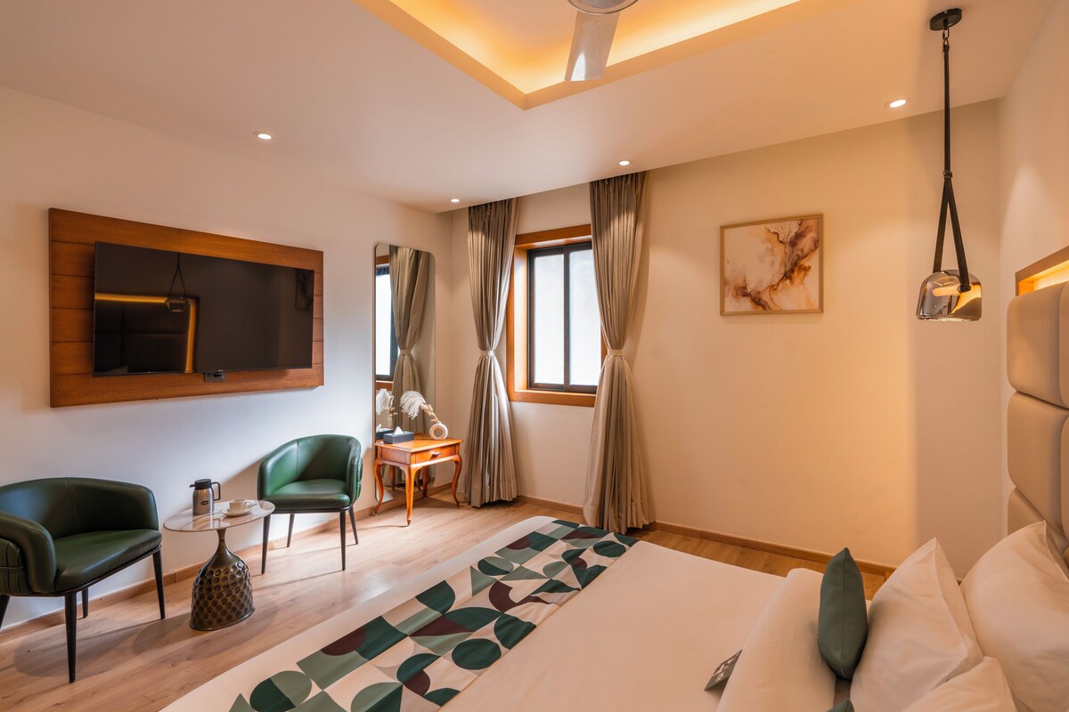 Una habitación de hotel moderna con una cama grande, un escritorio, dos sillas, un televisor y un cuadro en la pared.