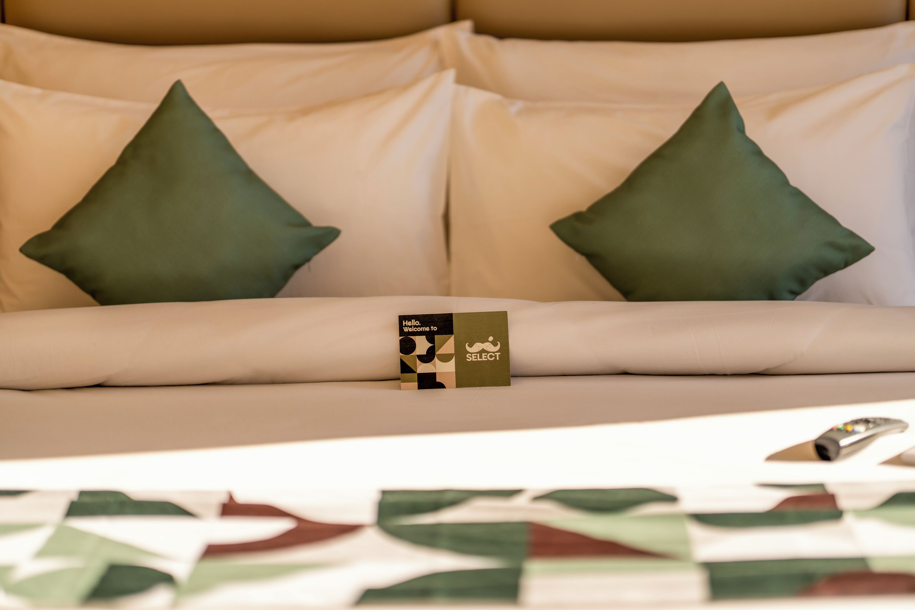 A bed with two pillows, a welcome card, and a remote control.