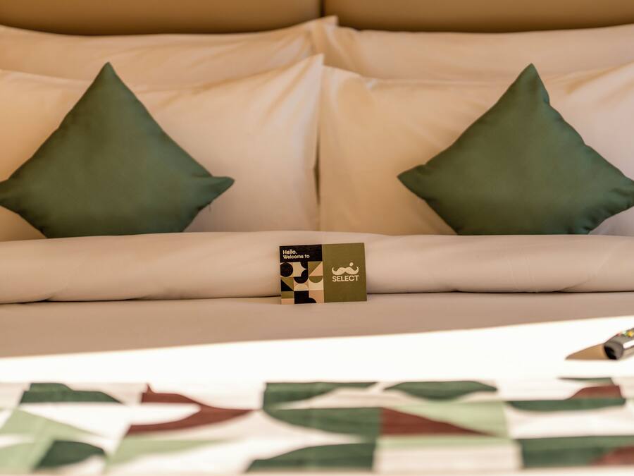 A bed with two pillows, a welcome card, and a remote control.