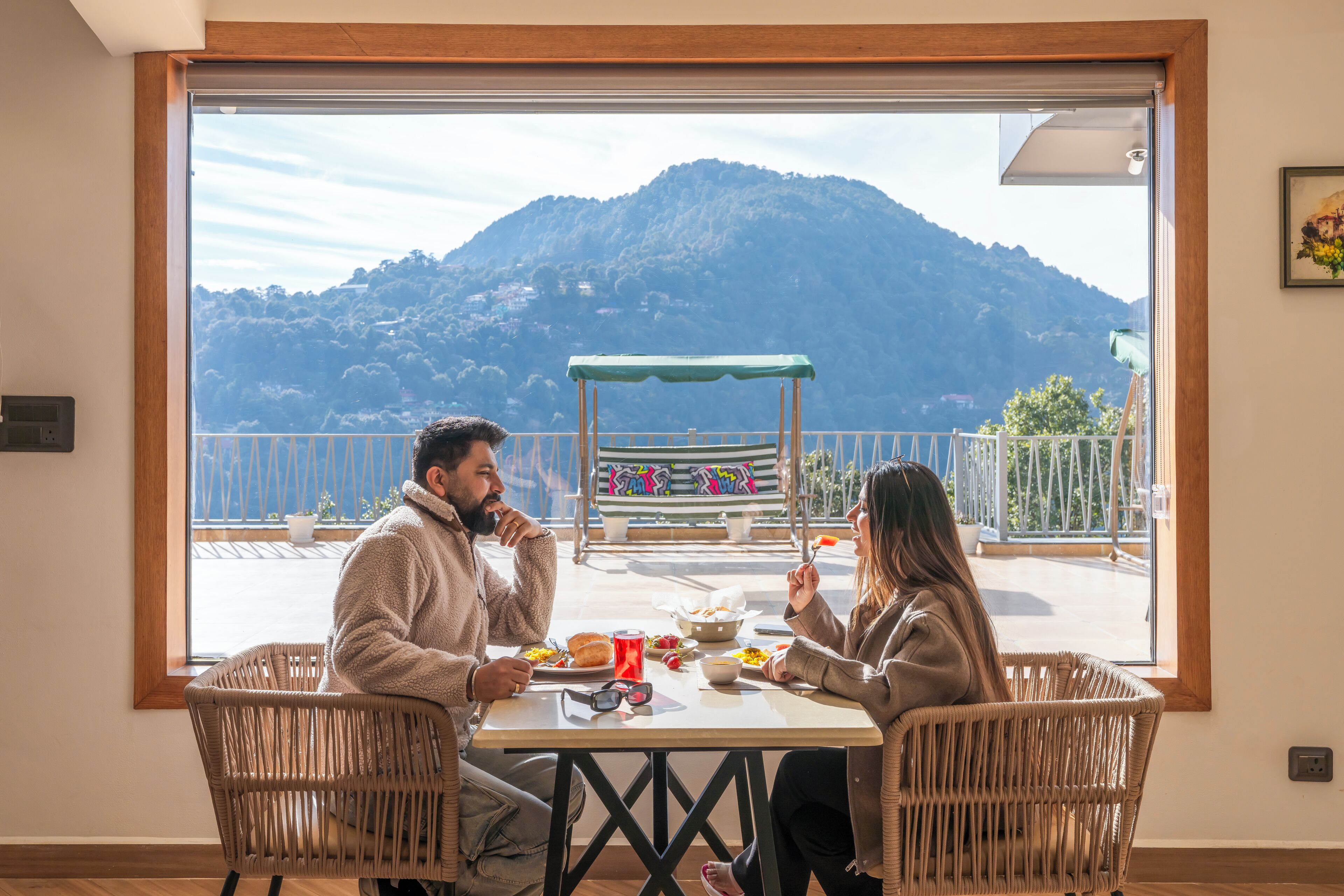 A dining area with a table and chairs, a view of a mountain, and a bench with colorful graffiti.