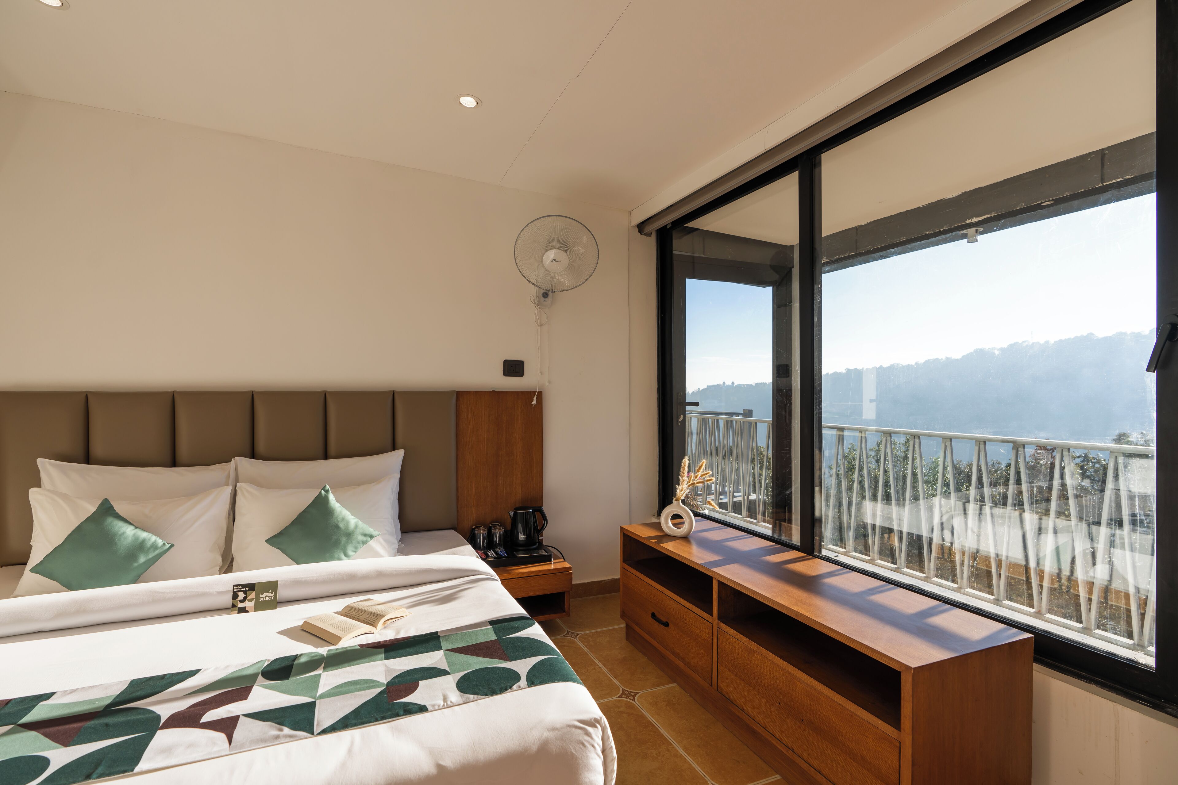 Ein Hotelzimmer mit einem großen Bett, einem Nachttisch, einer Holzkommode und einem Balkon mit Bergblick.
