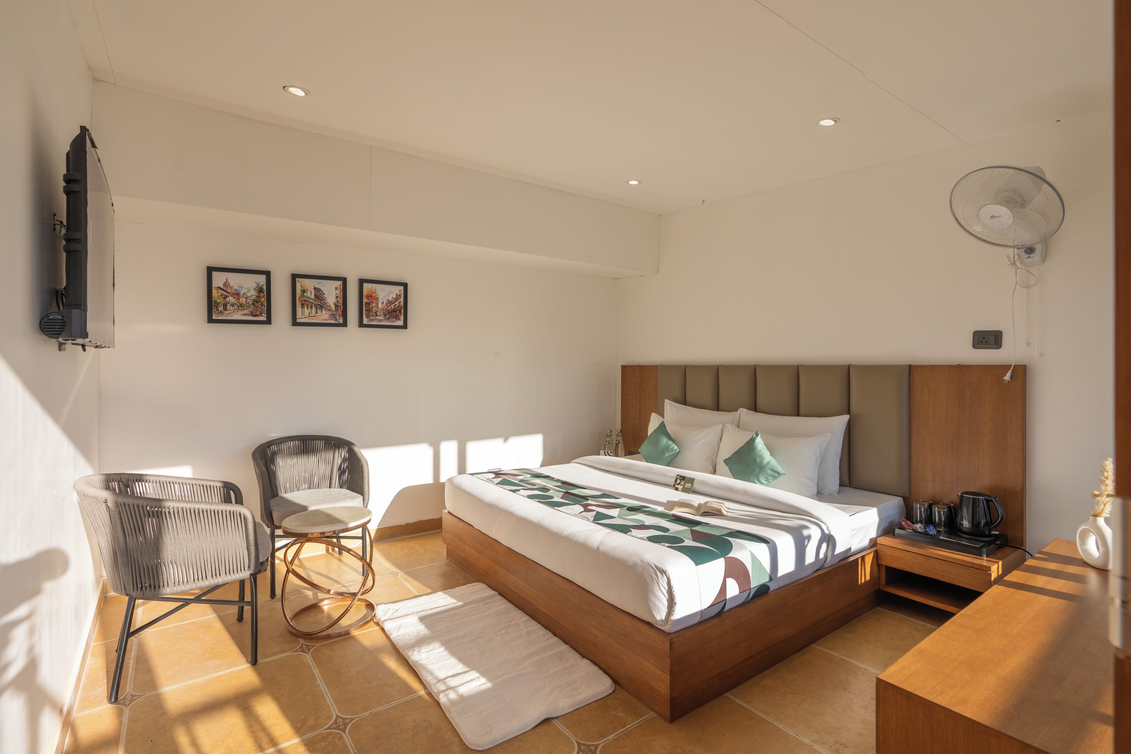 A modern bedroom with a large bed, a chair, a bedside table with a lamp, and a wall-mounted fan.