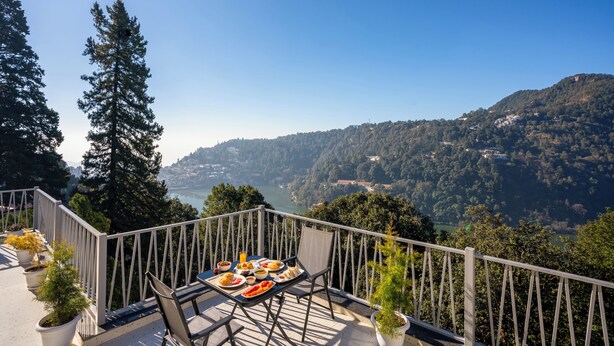 A balcony with a table set for a meal, overlooking a mountainous landscape and a body of water. - Moustache Select Nainital (Nainital, Uttarakhand)
