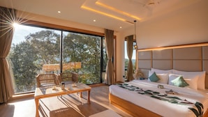 A modern bedroom with a large bed, a wooden coffee table, and a view of trees through large windows. - Moustache Select Nainital (Nainital, Uttarakhand)