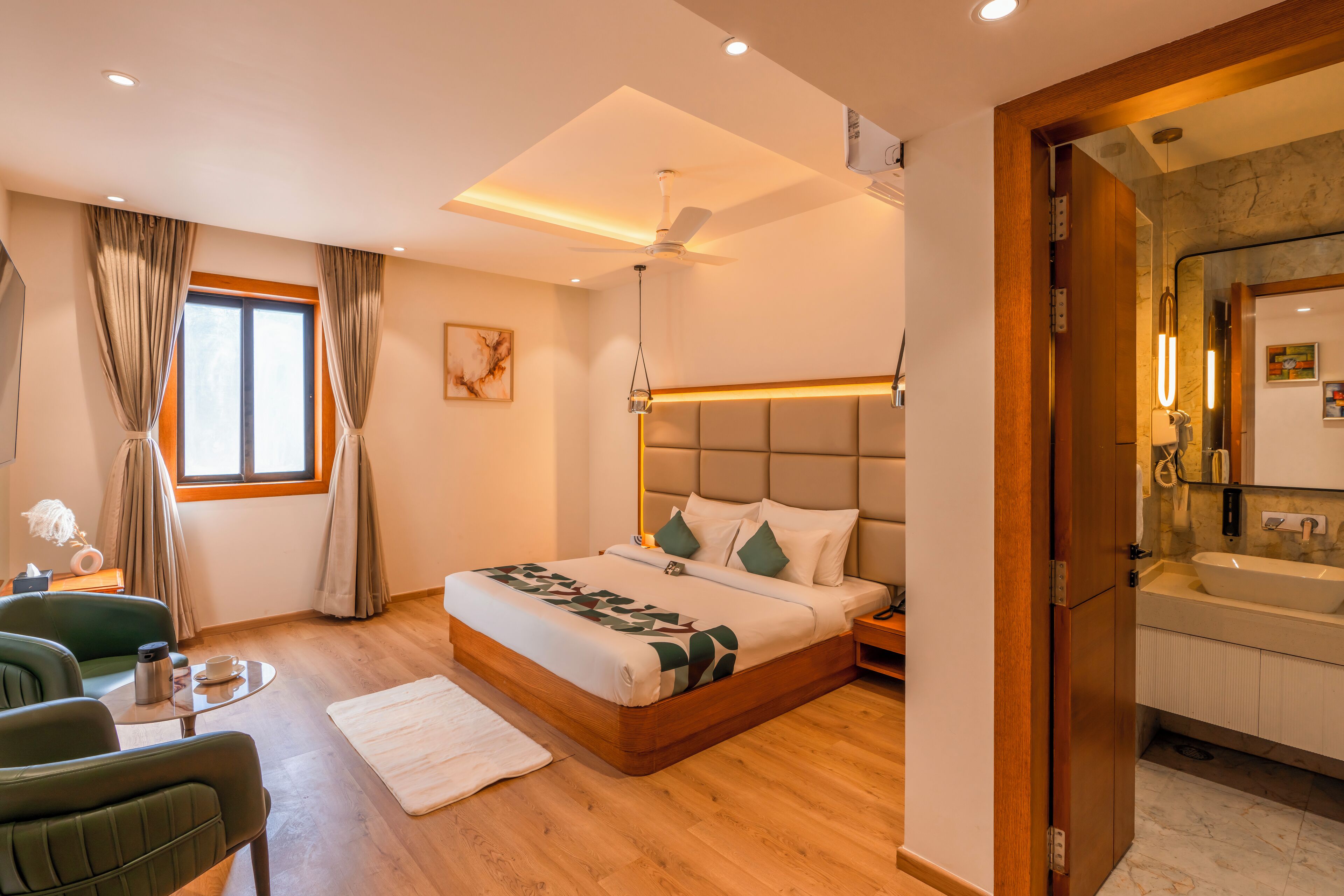 Un dormitorio moderno con una cama grande, una mesita de noche, una silla, una pequeña mesa con lámpara y una ventana con cortinas.