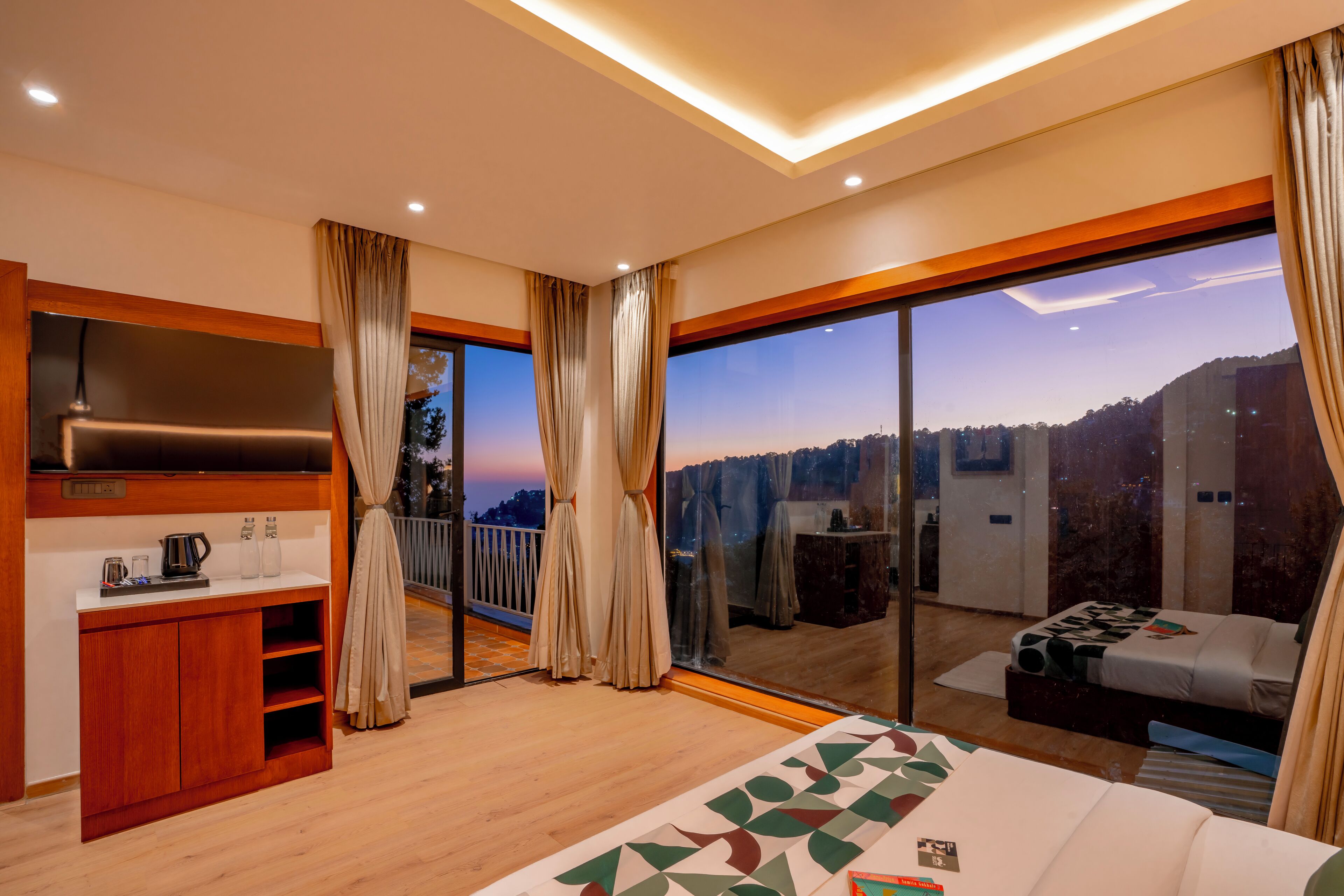 A modern hotel room with a large bed, a TV, a wooden cabinet, and a balcony with a city view.