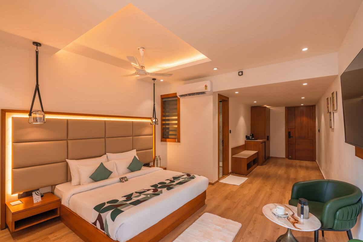 A modern hotel room with a large bed, a desk, a green armchair, and a TV.