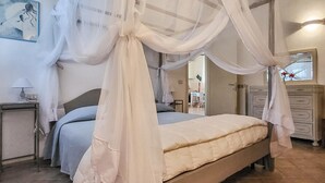 Um quarto com cama, mesa de cabeceira, abajur, cadeira, cômoda e um quadro na parede.