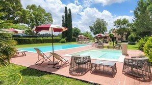 Piscina com espreguiçadeiras e guarda-sóis, rodeada por vegetação e um céu claro.