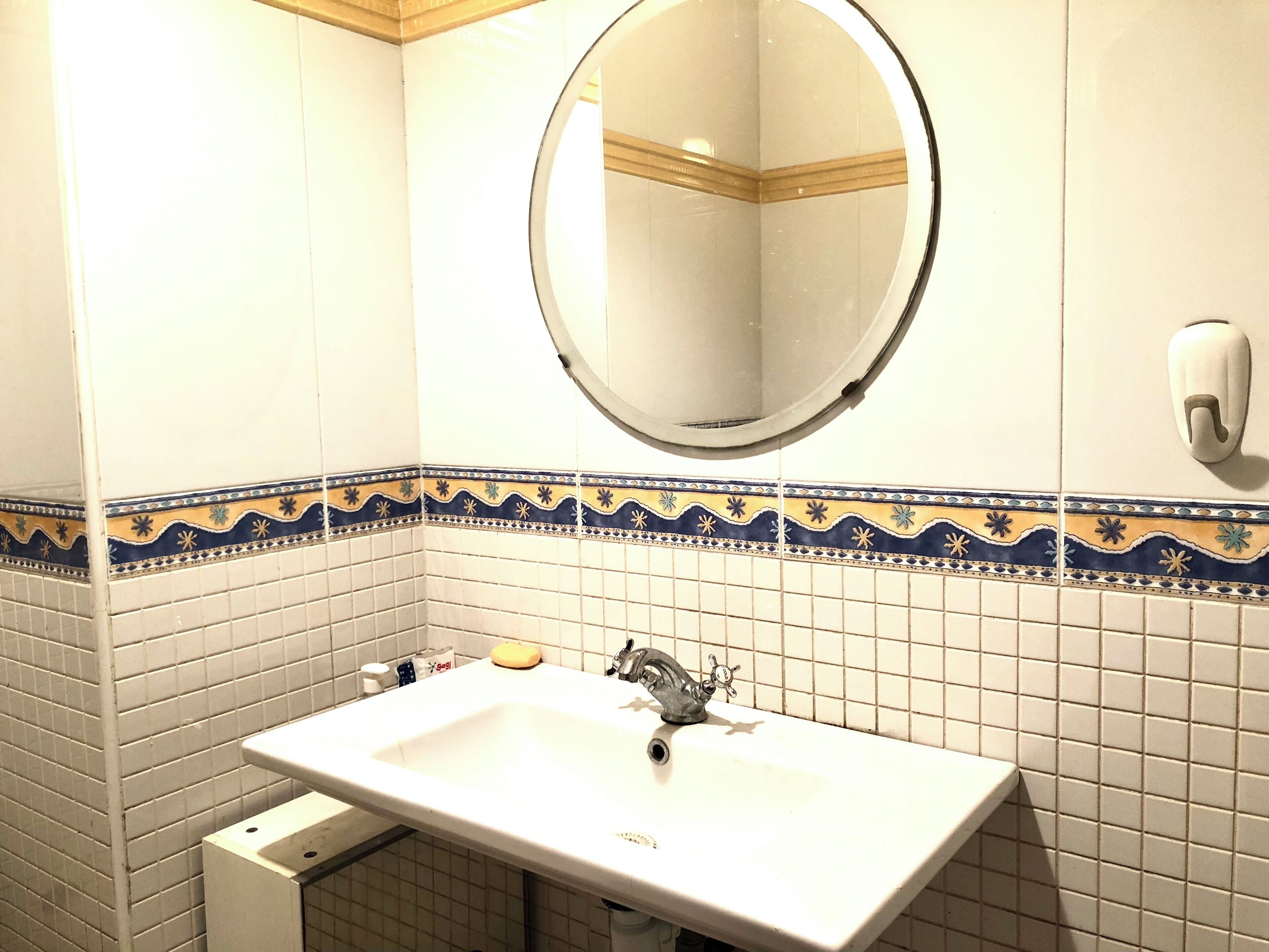 A bathroom with a white sink, a round mirror, and decorative blue and yellow tiles.