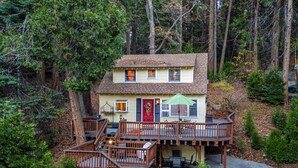 A two-story house with a deck, surrounded by trees.