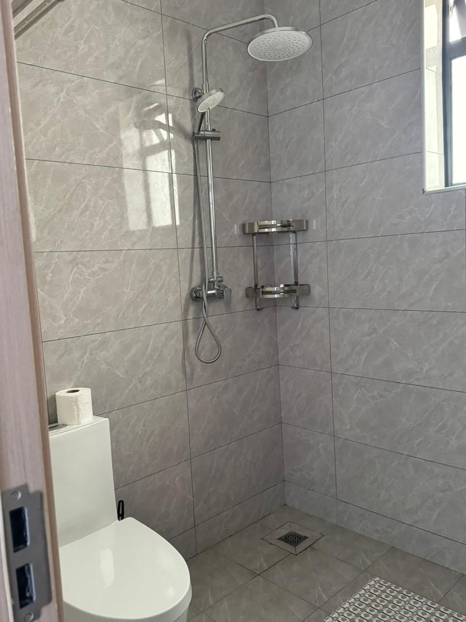 A small, modern bathroom with a shower, toilet, and a small window.
