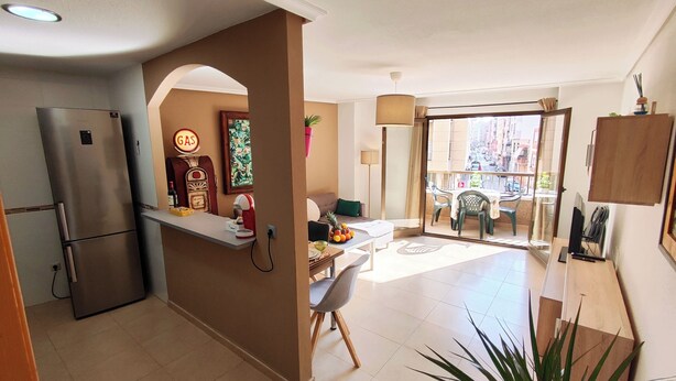 Eine kompakte Küche mit Kühlschrank, einer Kaffeemaschine und einer kleinen Arbeitsfläche. Ein Essbereich mit Tisch und Stühlen sowie ein Balkon mit Blick auf die Stadt.