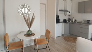 Cozinha moderna com armários brancos, micro-ondas e pia. Há uma área de refeições com uma mesa redonda e duas cadeiras.
