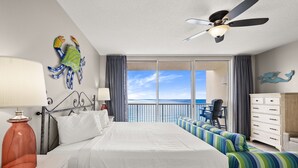 Ein Hotelzimmer mit einem großen Bett, einem Deckenventilator, Meerblick, einem Balkon mit einem Stuhl und einem Schminktisch.
