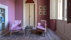 A room with two pink armchairs, a small table, a white cabinet with decorative items, a large arched doorway, and a window with a view. - Bubble Apartment - Villani Lubelli (Cannole)