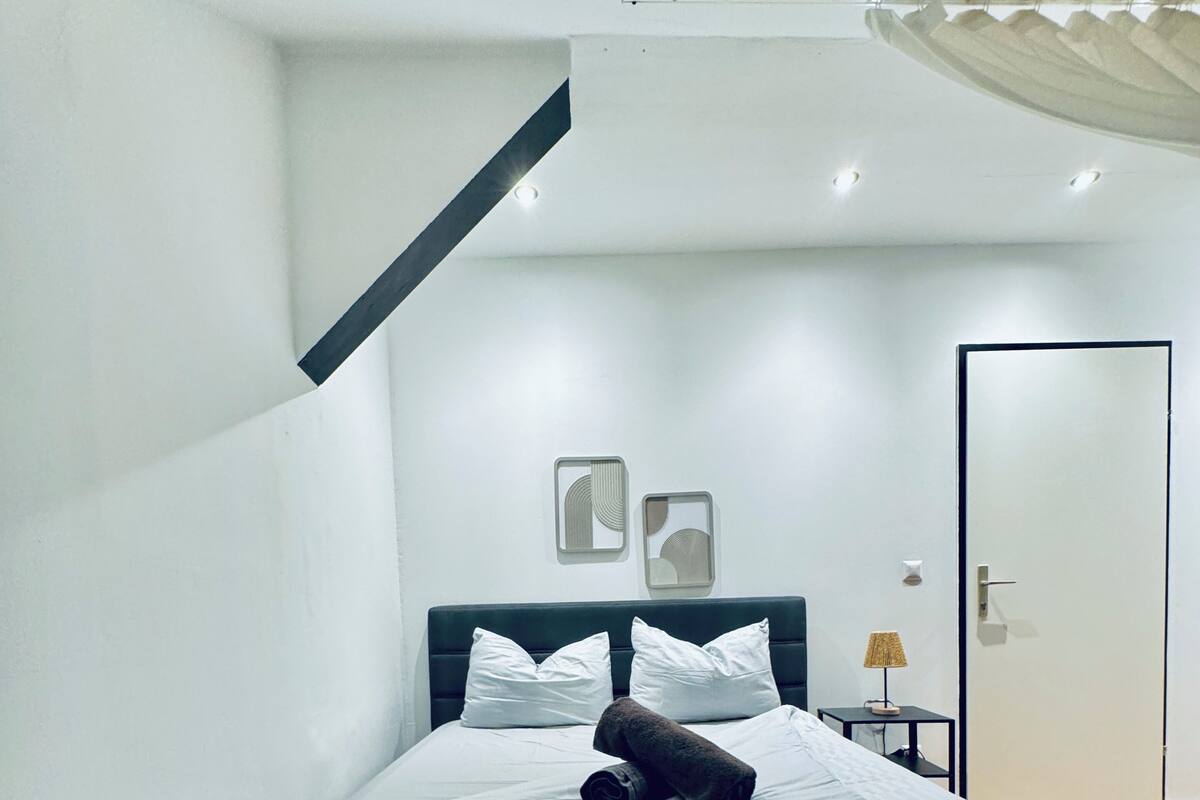 A modern bedroom with a large bed, a dark headboard, and a small bedside table with a lamp.