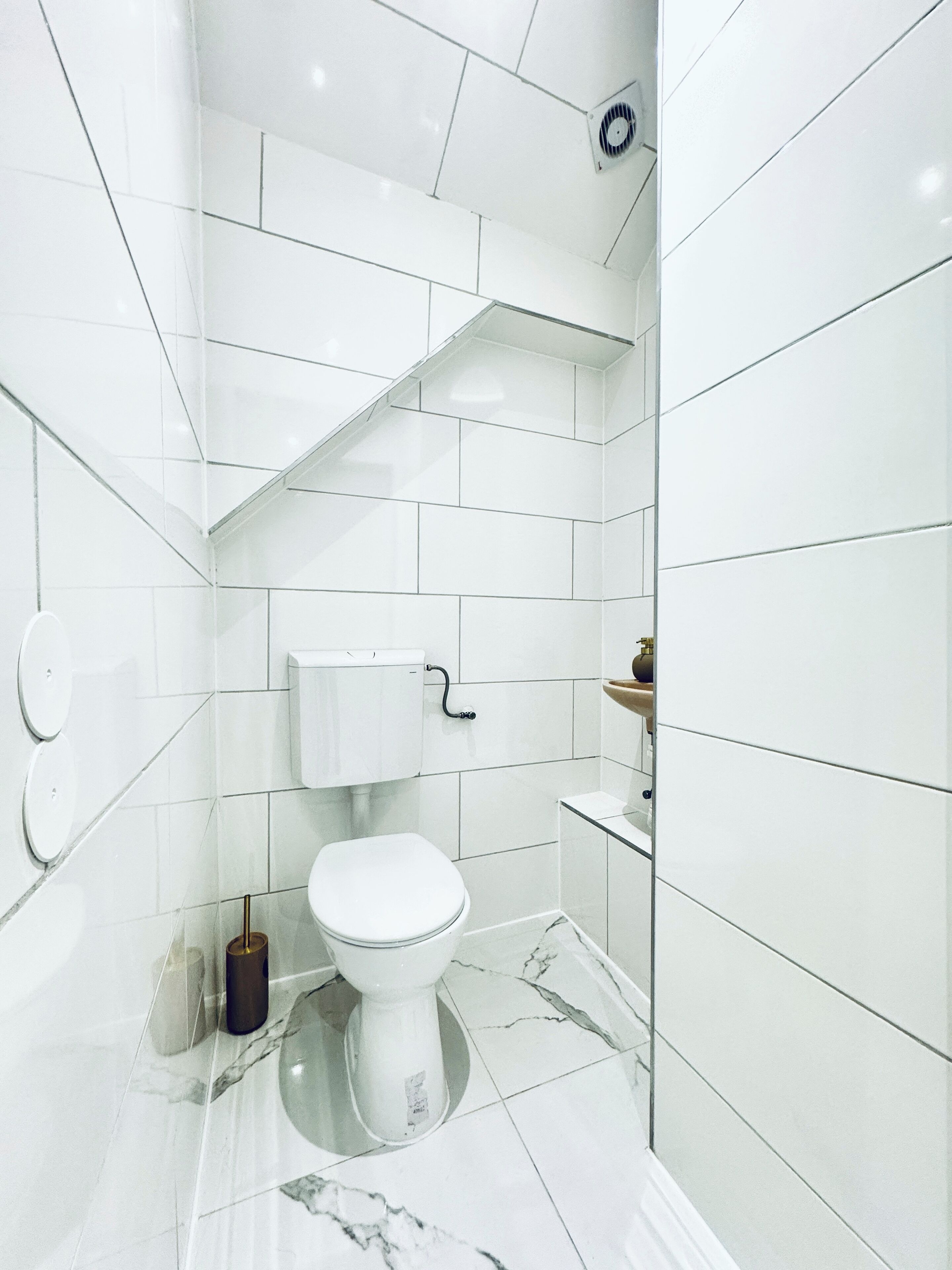 A modern bathroom with white tiles, a toilet, a sink, and a shower area.
