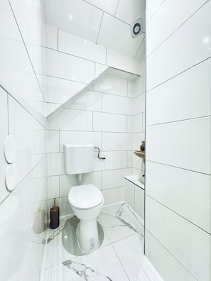 Ein modernes Badezimmer mit weißen Fliesen, einer Toilette, einem Waschbecken und einer Duschkabine.