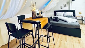 Un dormitorio moderno con una cama, una mesita, dos sillas y una planta decorativa.