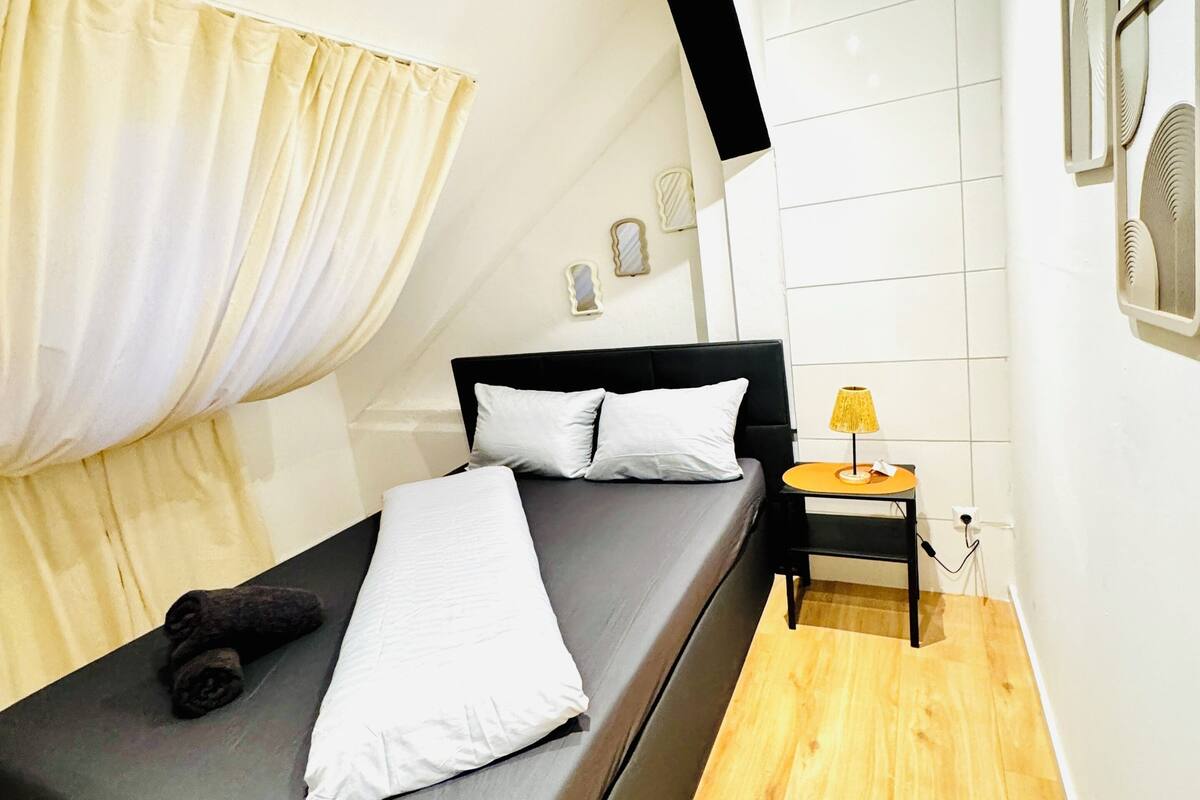 A modern bedroom with a bed, a nightstand, a lamp, and a wall-mounted mirror.