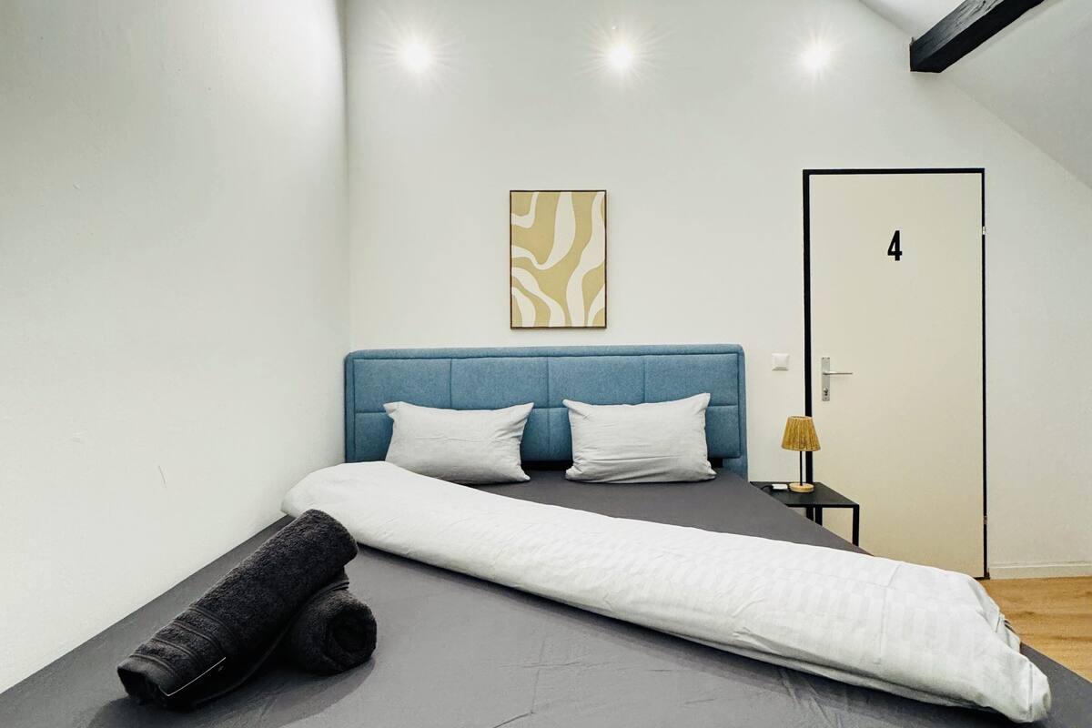 A modern bedroom with a sloped ceiling, a bed with a blue headboard, a wall-mounted artwork, and a door with the number 4.