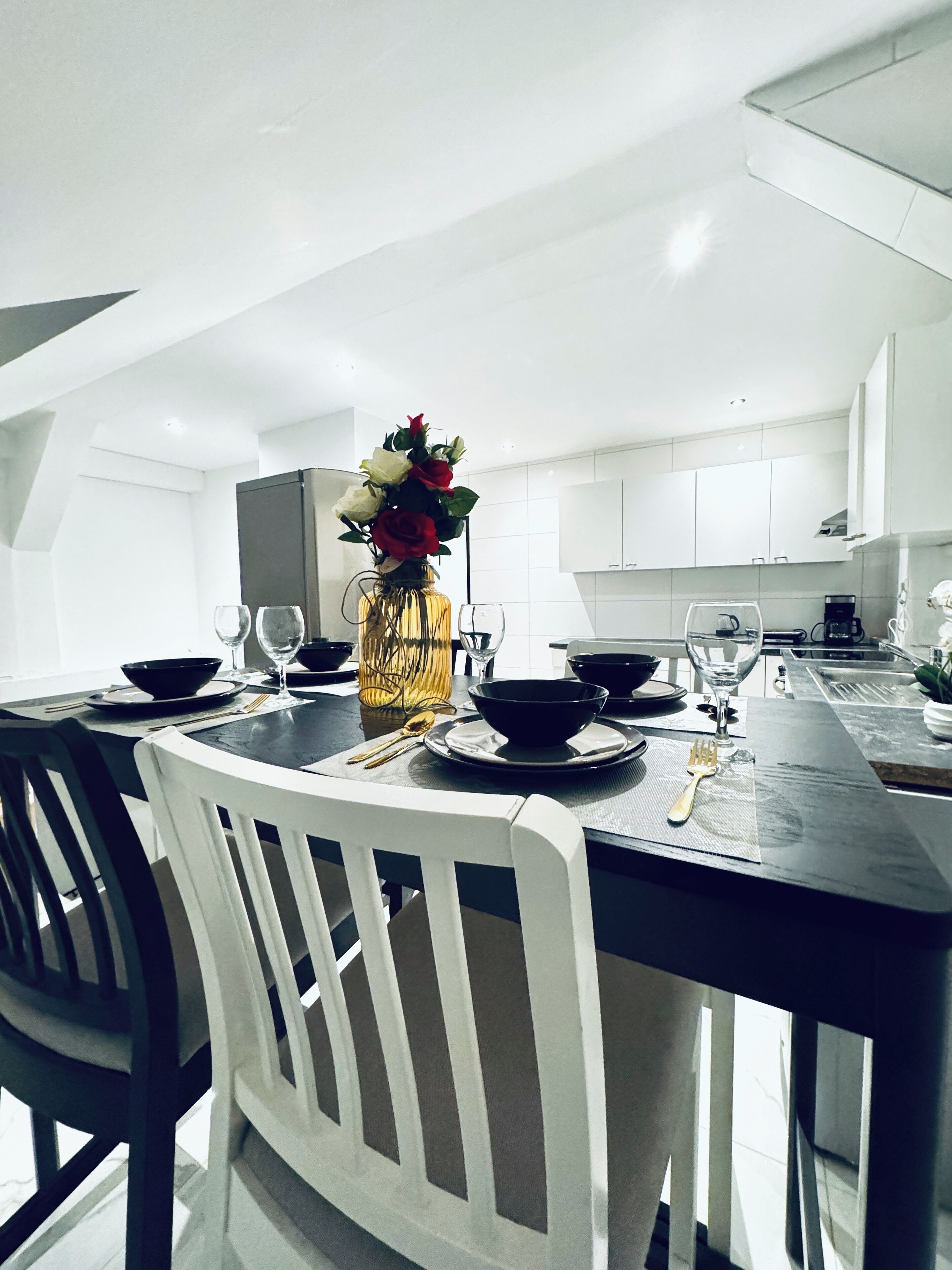 A modern kitchen with white cabinets, a dining table set for four, and a vase with flowers on the table.