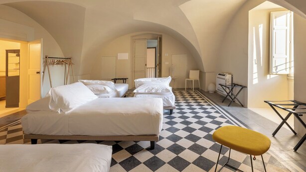 Een hotelkamer met een geruite vloer, twee bedden, een gele stoel, een tafel en een kledingkast.