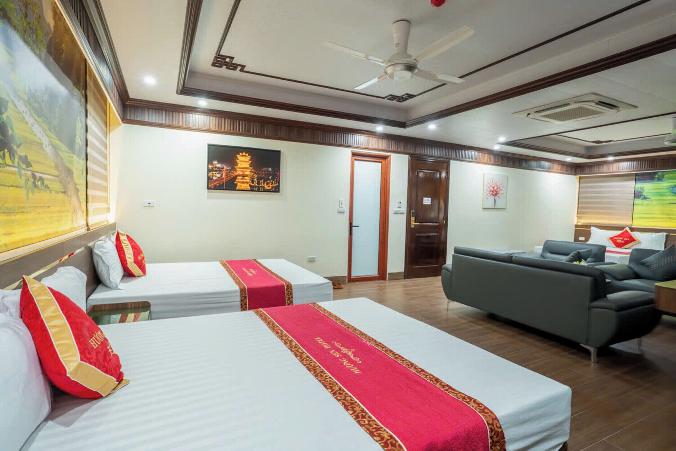 A hotel room with two beds, a sofa, a ceiling fan, and artwork on the walls.