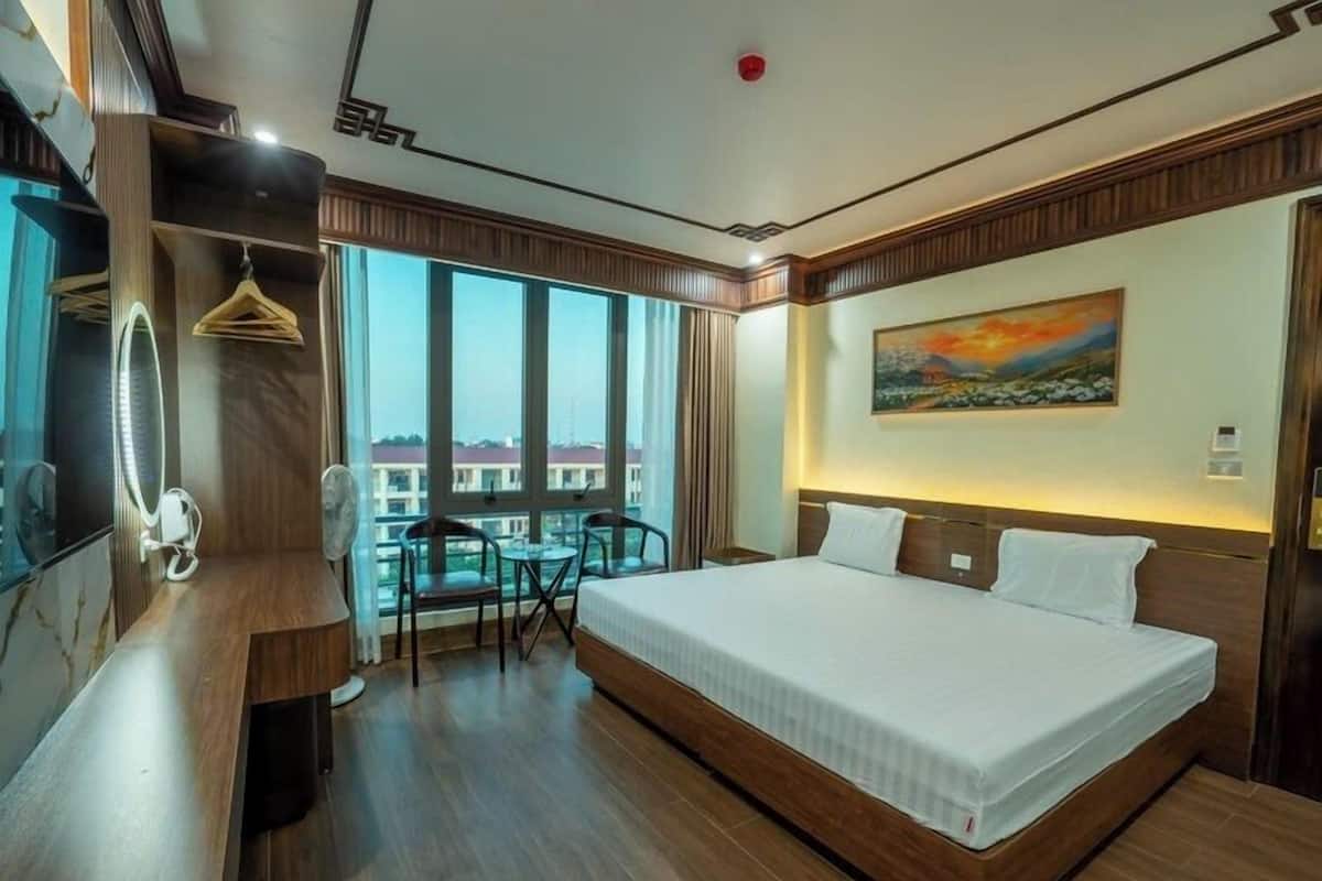 Une chambre d’hôtel avec un grand lit, un bureau avec une chaise, une petite table avec deux chaises, un miroir et un tableau au mur.