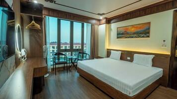 A hotel room with a large bed, a desk with a chair, a small table with two chairs, a mirror, and a painting on the wall.