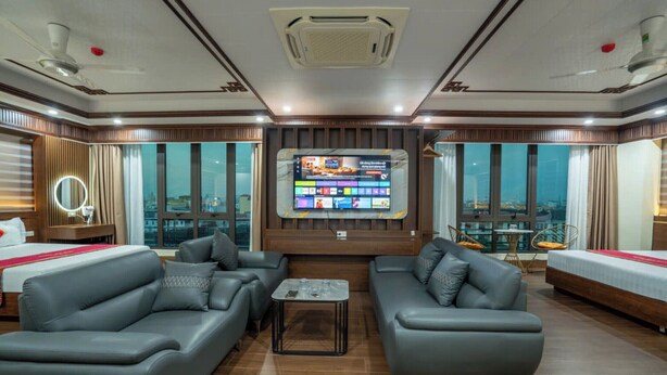Ein modernes Hotelzimmer mit großem Fernsehbildschirm, Ledersofas, einem kleinen Couchtisch und Blick auf die Stadt durch große Fenster.