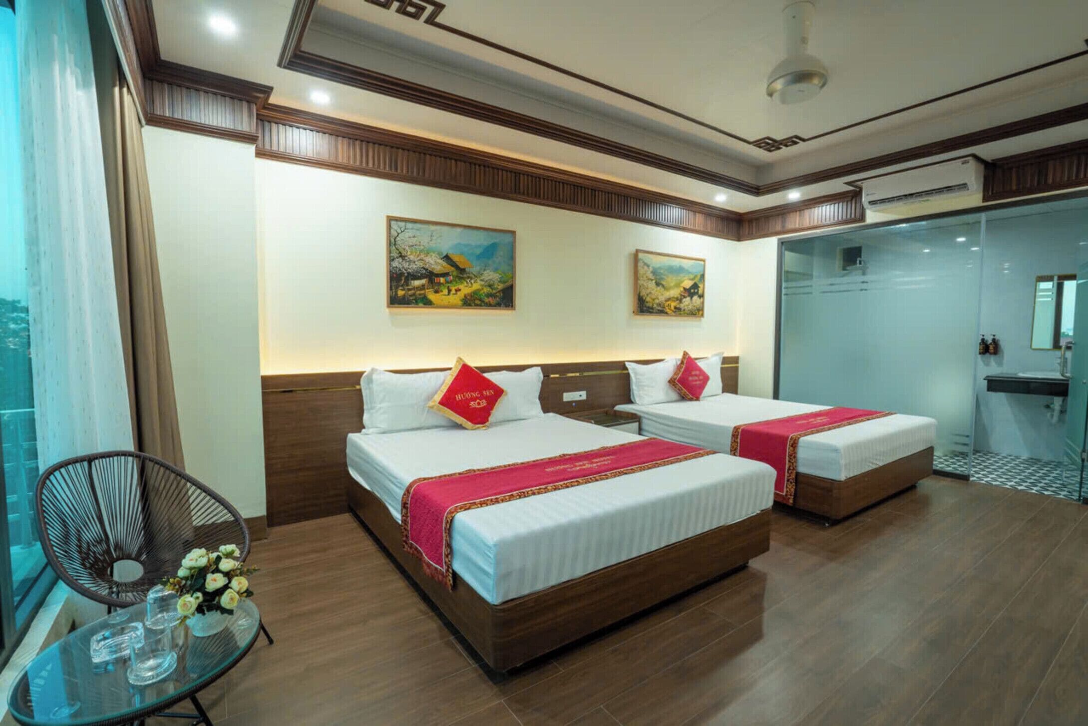 A hotel room with two beds, a glass table with drinks, and artwork on the wall.