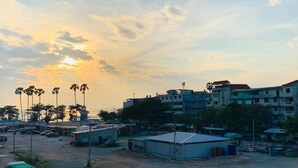 A coastal urban area with buildings, a sandy ground, and palm trees under a sunset sky. - Sea Prestige (Pattaya)