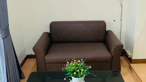 A living room with a brown sofa, a glass-top table, and a potted plant. - Sea Prestige (Pattaya)