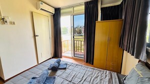 A bedroom with a bed, a wardrobe, a sliding glass door to a balcony, and an air conditioning unit. - Sea Prestige (Pattaya)