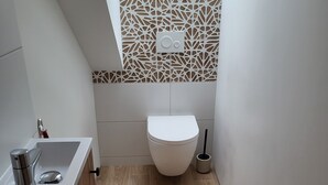 Casa de banho pequena e moderna com sanita, lavatório e um painel decorativo na parede.