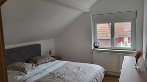 Quarto com cama, mesa de cabeceira, janela e radiador.