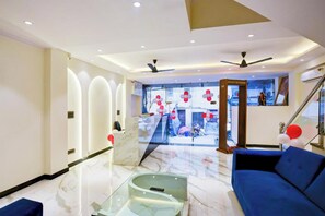 Een moderne hotel lobby met een blauwe bank, een glazen bijzettafeltje en een plafondventilator.